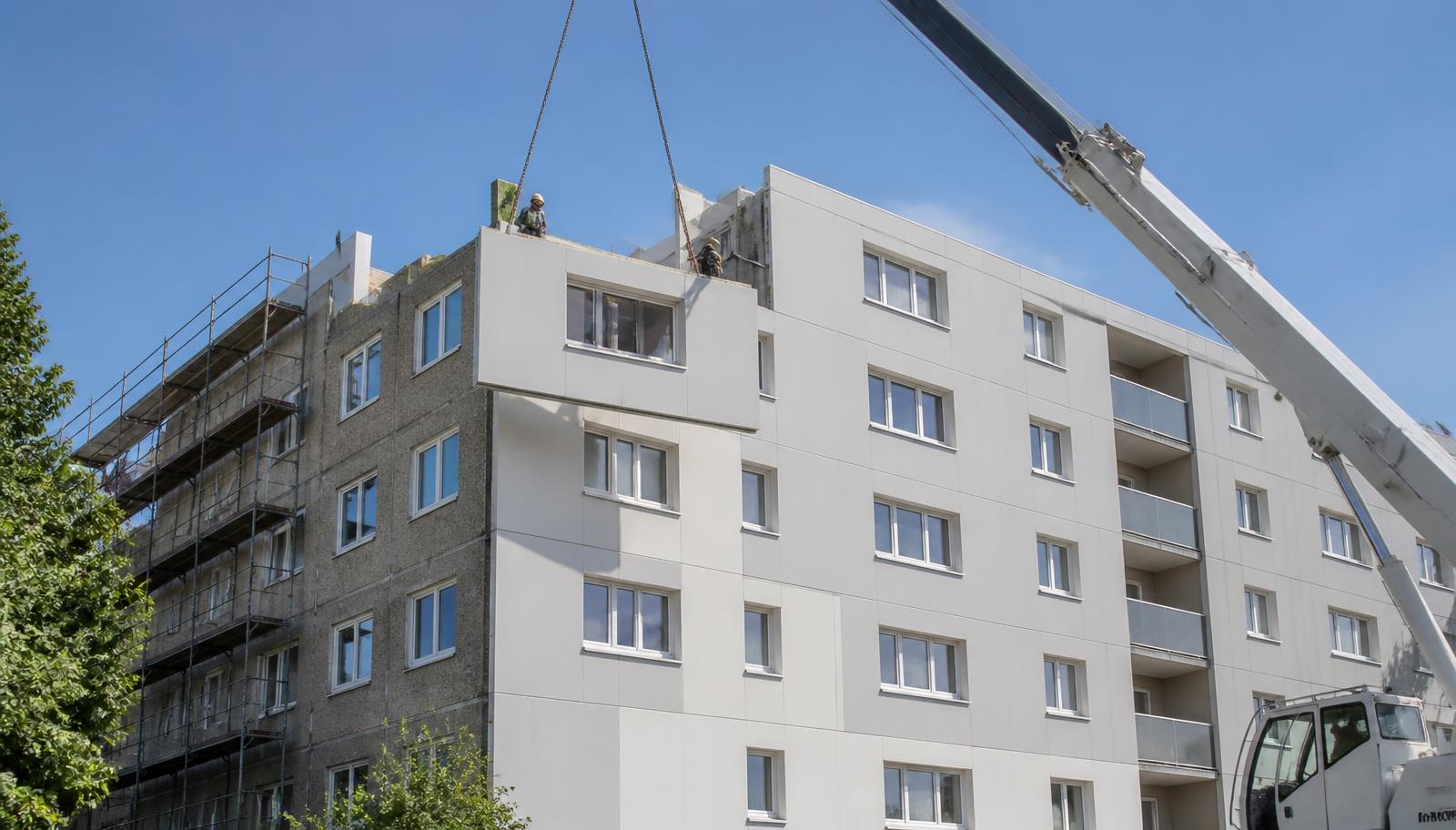 Kran hebt ein vorgefertigtes Fassadenelement an ein Mehrfamilienhaus